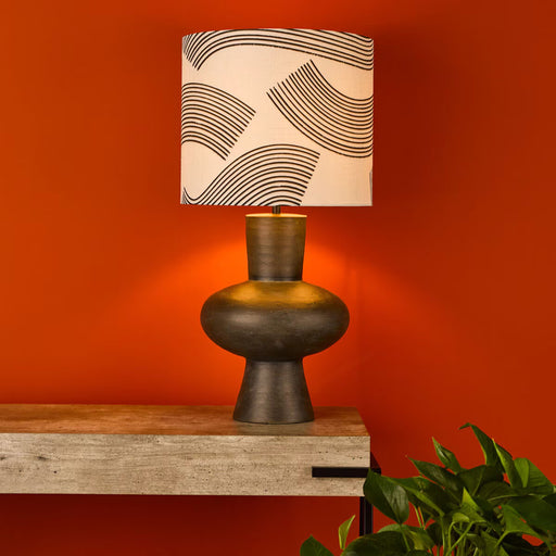 table lamp with bulbous resin base and patterned linen and black fabric shade on side table